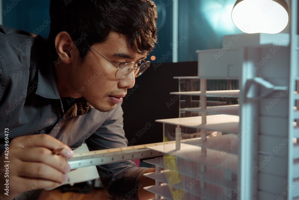 Poster architect-designer working at night with model of hight building while thinking about concept of bui