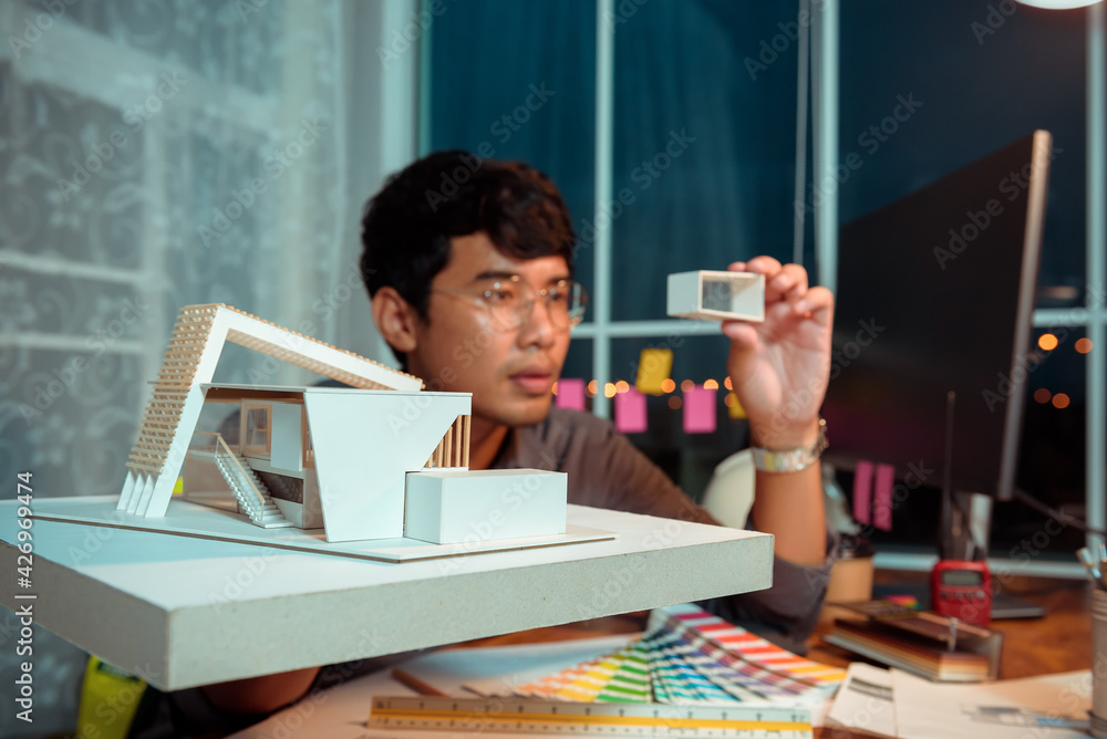 Poster architect-designer working at night with model of modern box house while thinking about concept of b