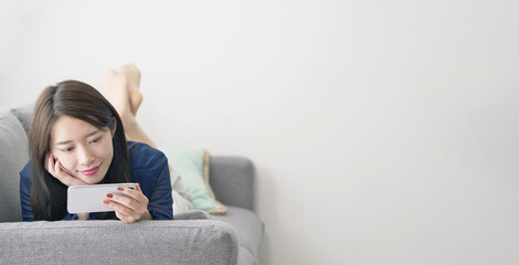 ソファに寝転がってスマホを見る女性