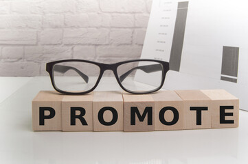 The word PROMOTION is written on wooden cubes next to glasses and a document on the office desk