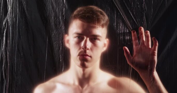 Man loneliness. Defocused portrait. Social isolation. Sorrow regret. Unhappy sad pensive shirtless guy looking through creased texture polyethylene film on dark background out of focus.