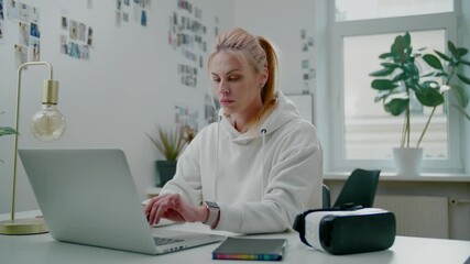 Calm fair haired student types on modern laptop in room