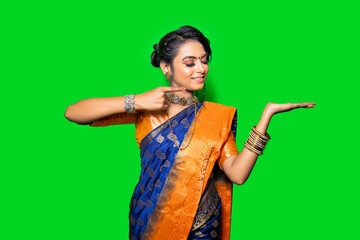 Indian woman in saree presenting or pointing finger at copy space at palm isolated over green background