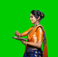 Beautiful Traditional Indian young woman holding pooja thali or performing worship on a green...