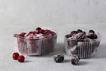 Two containers with frozen blackberries and cherries on the gray background. Harvesting berries for the winter.