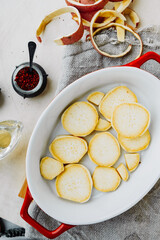 round slices raw red sweet potatoes in red ceramic baking dish, spices, salt, pepper, potato peel. process cooking homemade food. yam recipes, vertical food content, life atmosphere, selective focus