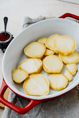 kitchen table with spices for cooking homemade yam food.salt, paprika and round slices of raw red sweet potato in red ceramic baking dish, vertical food content, life atmosphere, selective focus