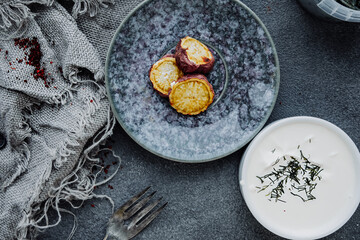 baked chopsticks sweet potato slices in porcelain mug in dark kitchen with white cream sauce on rough burlap gray napkin. quick homemade yam recipes. country food. selective focus