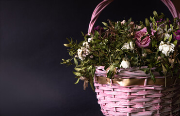 Bouquet of various flowers and leaves into pink basket on a dark background with copy space