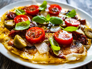 Delicious breakfast - scrambled eggs with onion, sun dried tomato, basil, parmesan and green olives on wooden table
