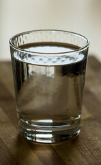 Close up of a glass of still water on used striped wooden mat.
