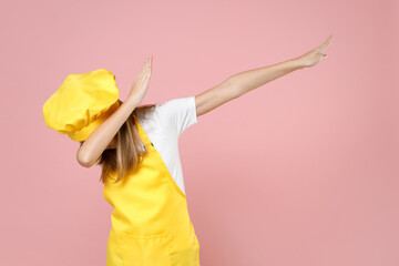 Teen girl chef cook confectioner baker housewife in yellow apron white t-shirt cap do dab hip hop dance hands move gesture youth sign hiding cover face isolated on pink background Food cake concept.