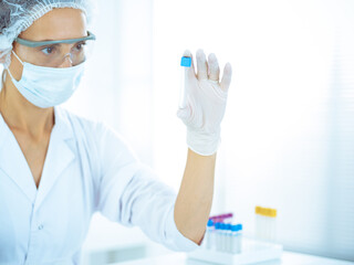 Professional female scientist in protective eyeglasses researching tube with reagents in laboratory...