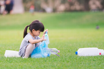 Asian girl is packing plastic bottle in bag. Children collect garbage to help maintain clean and...