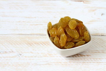 Yellow raisins are in a white bowl on a white wooden table. Raisins  healthy snacks