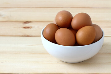 Organic eggs in a white bowl are placed on a wooden table.