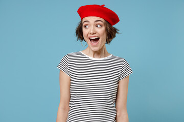 Young surprised excited caucasian overjoyed woman 20s with short hairdo in french beret red hat striped t-shirt spread hands isolated on pastel blue background studio portrait People lifestyle concept