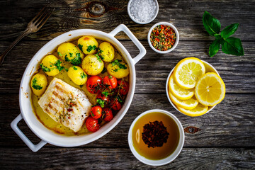 Fish dish - baked cod fillet with potatoes and cherry tomatoes on wooden table
