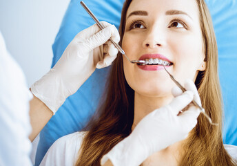 Smiling young woman with orthodontic brackets examined by dentist in dental clinic. Healthy teeth and medical care concept