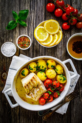 Fish dish - baked cod fillet with potatoes and cherry tomatoes on wooden table
