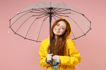 Redhead young woman in yellow waterproof raincoat hood outerwear hold transparent umbrella isolated...