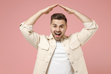 Young happy satisfied friendly caucasian man in jacket white tshirt hold folded hands above head like house roof, stay home isolated on pastel pink background studio portrait People lifestyle concept.