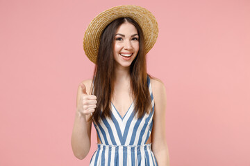 Young excited positive cheerful caucasian woman in summer clothes striped dress straw hat show thumbs up like gesture blink isolated on pastel pink background studio portrait People lifestyle concept