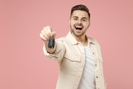 Young successful smiling excited caucasian fun happy man 20s wear jacket white t-shirt giving car fob keys keyless system isolated on pastel pink background studio portrait. People lifestyle concept.