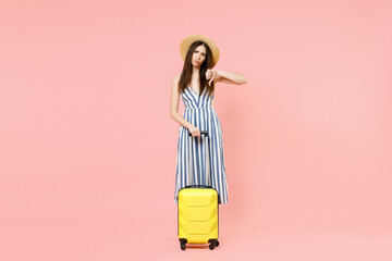 Full length traveler tourist woman in summer clothes, hat hold yellow suitcase show thumb down isolated on pastel pink background Passenger travel abroad weekends getaway Air flight journey concept.