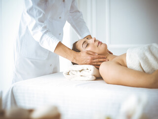 Obraz na płótnie Canvas Beautiful brunette woman enjoying facial massage with closed eyes comfortable and blissful. Relaxing treatment in medicine and spa center concepts