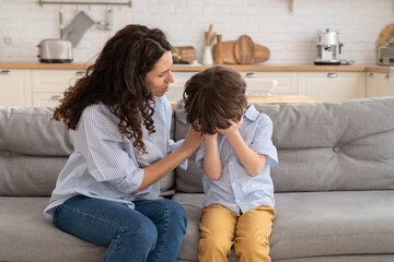 Closeup of worried mother calm weeping kid. Upset little boy cry sit on couch together with caring...