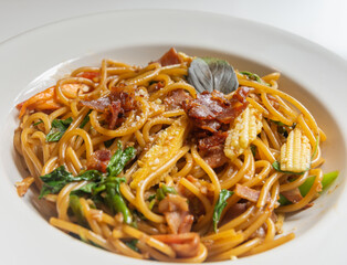 Spicy spaghetti with bacon and basil in the white dish.
