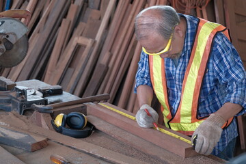Old Asian man carpenter working in a woodworking factory. They are using a tape measure and a...