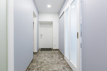 Interior photography, corridor of a small apartment in a modern minimalist style, with white walls, sliding doors, and black marble tiles on the floor