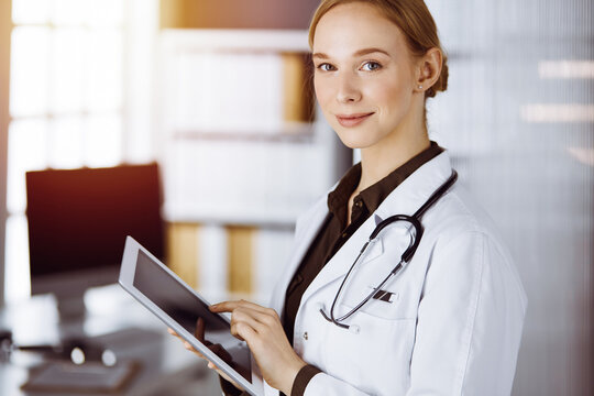 Cheerful smiling female doctor using clipboard in clinic. Portrait of friendly physician woman at work. Medical service in hospital. Medicine concept