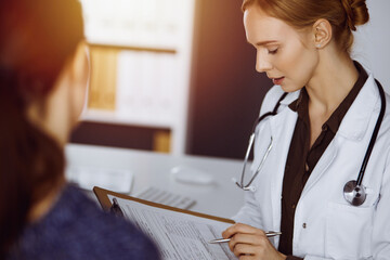 Cheerful smiling female doctor and patient woman discussing current health examination while...