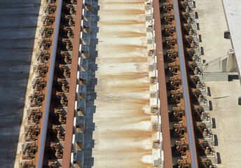 High angle view of metro rail tracks on concrete under sun. Details of concrete work, jolts, joints and rusted rails are seen.