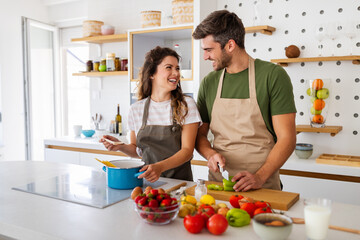 Obraz na płótnie Canvas Young happy couple is enjoying and preparing healthy meal in their kitchen