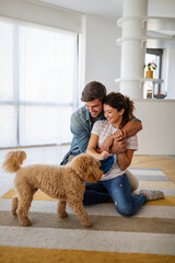 Cheerful young loving couple is playing with their dog at home.