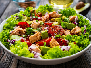 Tuna salad - tuna, cherry tomatoes, avocado, lettuce and onion on wooden table
