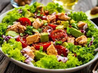 Tuna salad - tuna, cherry tomatoes, avocado, lettuce and onion on wooden table
