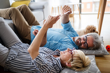 Obraz premium Beautiful happy mature couple is using a digital tablet, talking and smiling at home