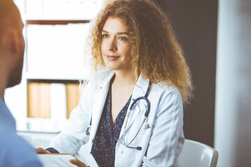 Female doctor and male patient discussing current health examination while sitting in sunny clinic