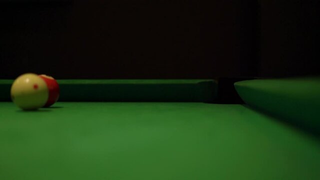 Heavy colorful billiard balls with numbers roll along pool table covered with green velvet fabric in semi-dark bar hall extreme closeup.