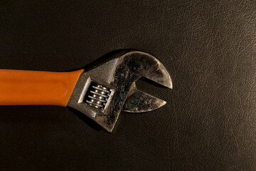 Top view close up of the head of an adjustable wrench with plastic orange handle, lying on leather surface.