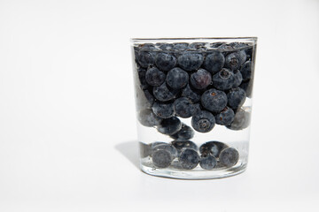 Crockery with juicy and fresh blueberries on white table.Close up portrait of fresh blueberries in a glass bowl on white background