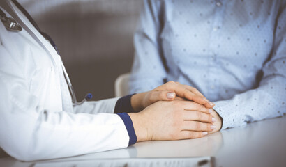 Unknown woman-doctor is holding her patient's hands to reassure a patient, while sitting together...
