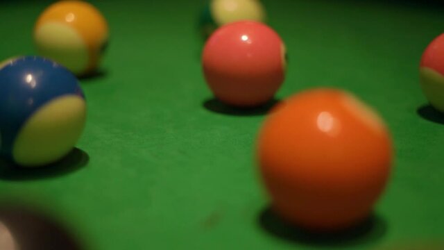 Set of colorful billiard balls with numbers lies on modern pool table covered with green velvet fabric in semi-dark bar hall extreme closeup.