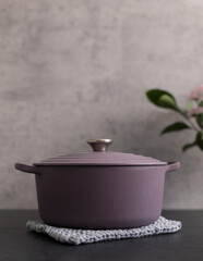 Round lilac rustic cast iron casserole on a knitted blue cloth over a gray background.
