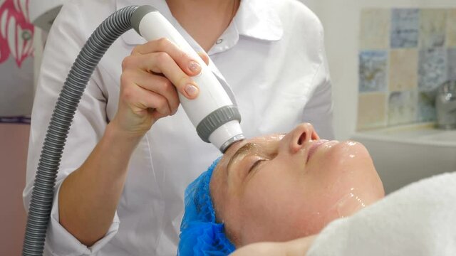 Facial lifting, wrinkle smoothing and rhytide effacement procedure. Hardware cosmetology treatment. Beautician moves manipulator with light on aged female face. Non-surgical face skin lifting in